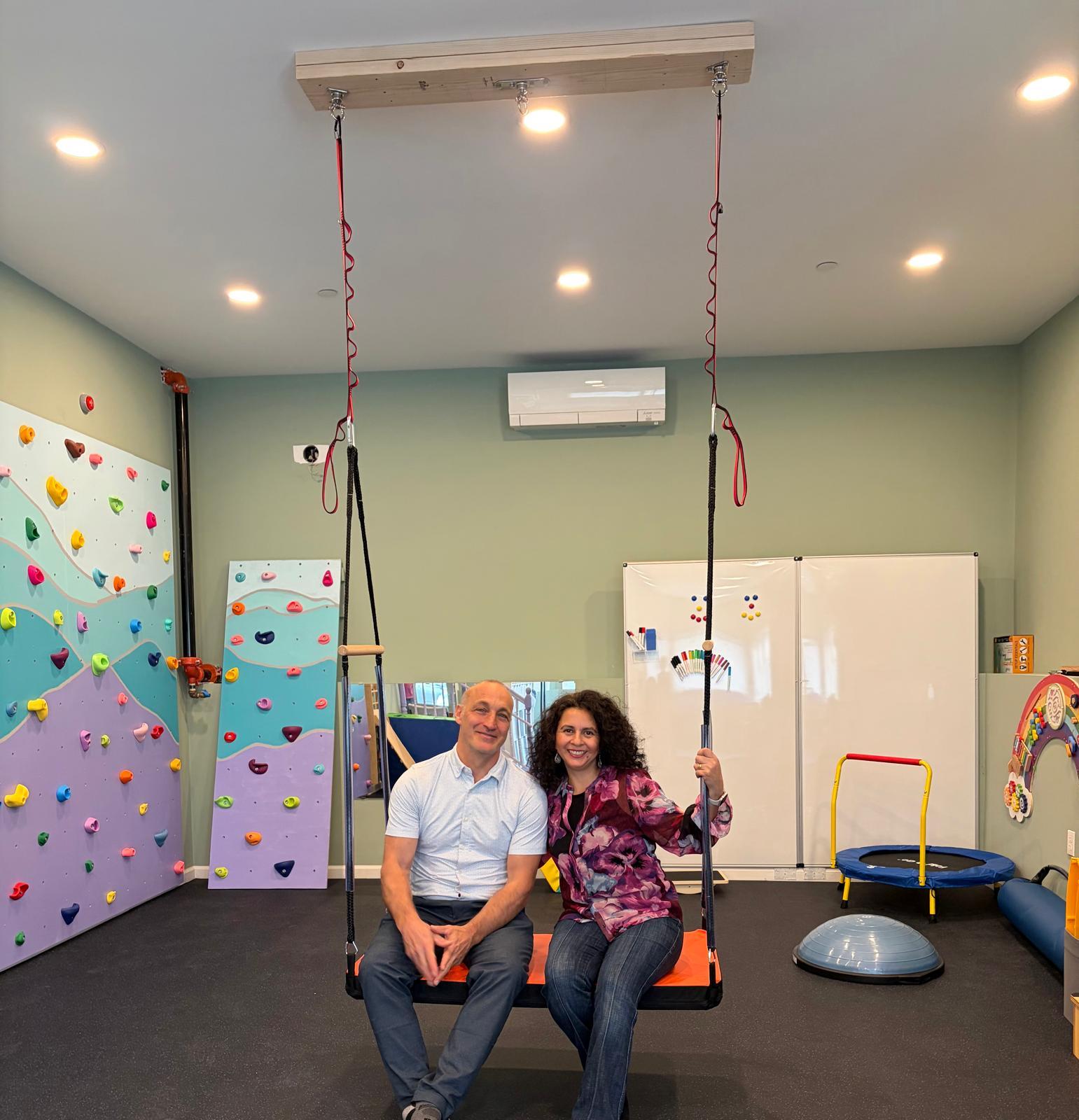 A therapist speaking warmly with a parent while a child plays nearby